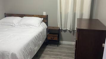 A bedroom with a bed, a nightstand, a wooden cabinet, and a wall-mounted power outlet.