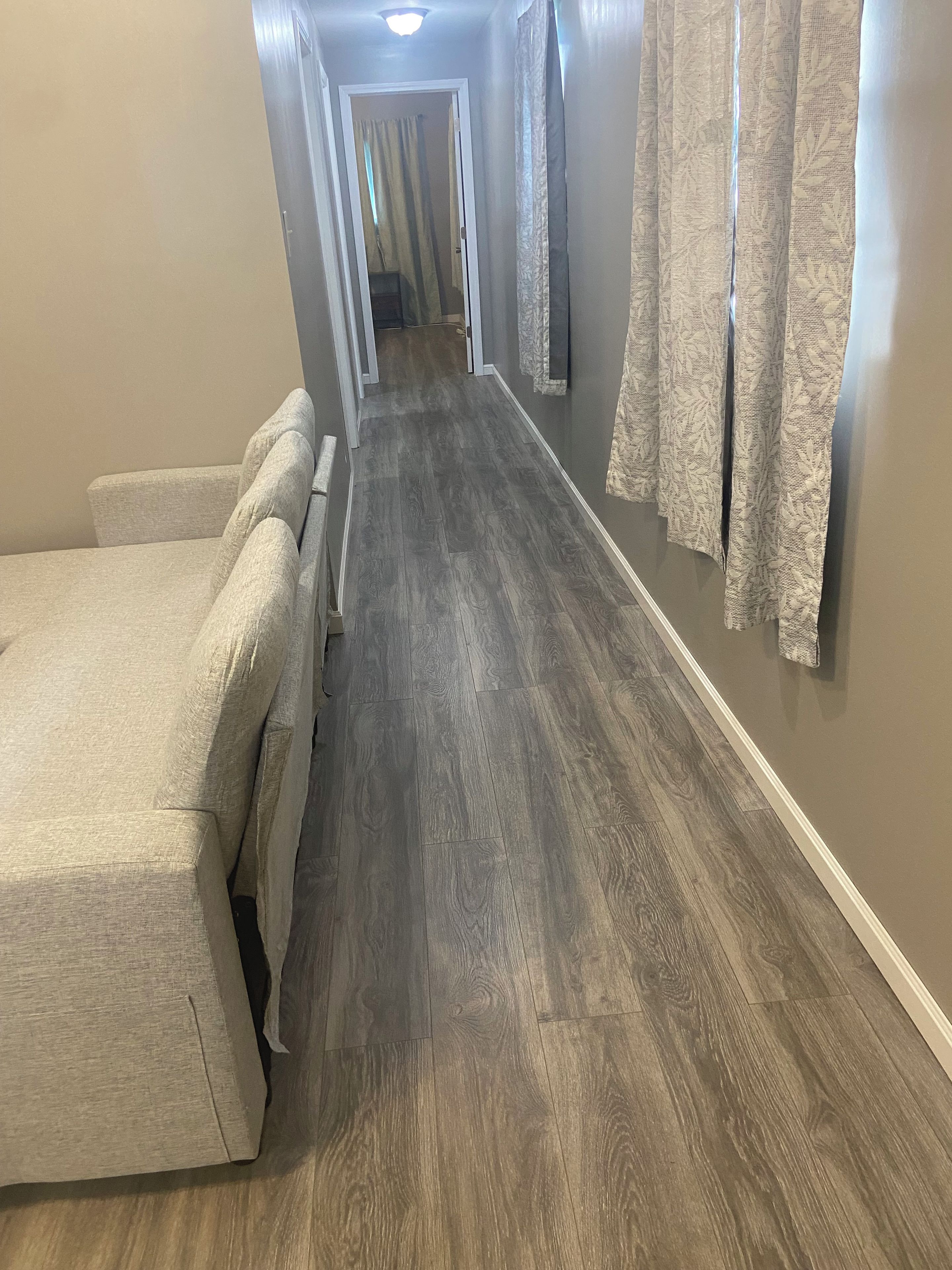 A hallway with a bed on the left, a wooden floor, and curtains on the right.