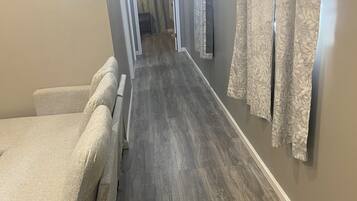 A hallway with a bed on the left, a wooden floor, and curtains on the right.