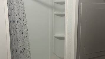 A bathroom with a shower curtain, a toilet, and a wall-mounted shelf.