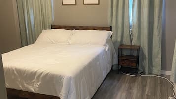 Un dormitorio con una cama de madera, cortinas verde claro y dos láminas botánicas enmarcadas en la pared.