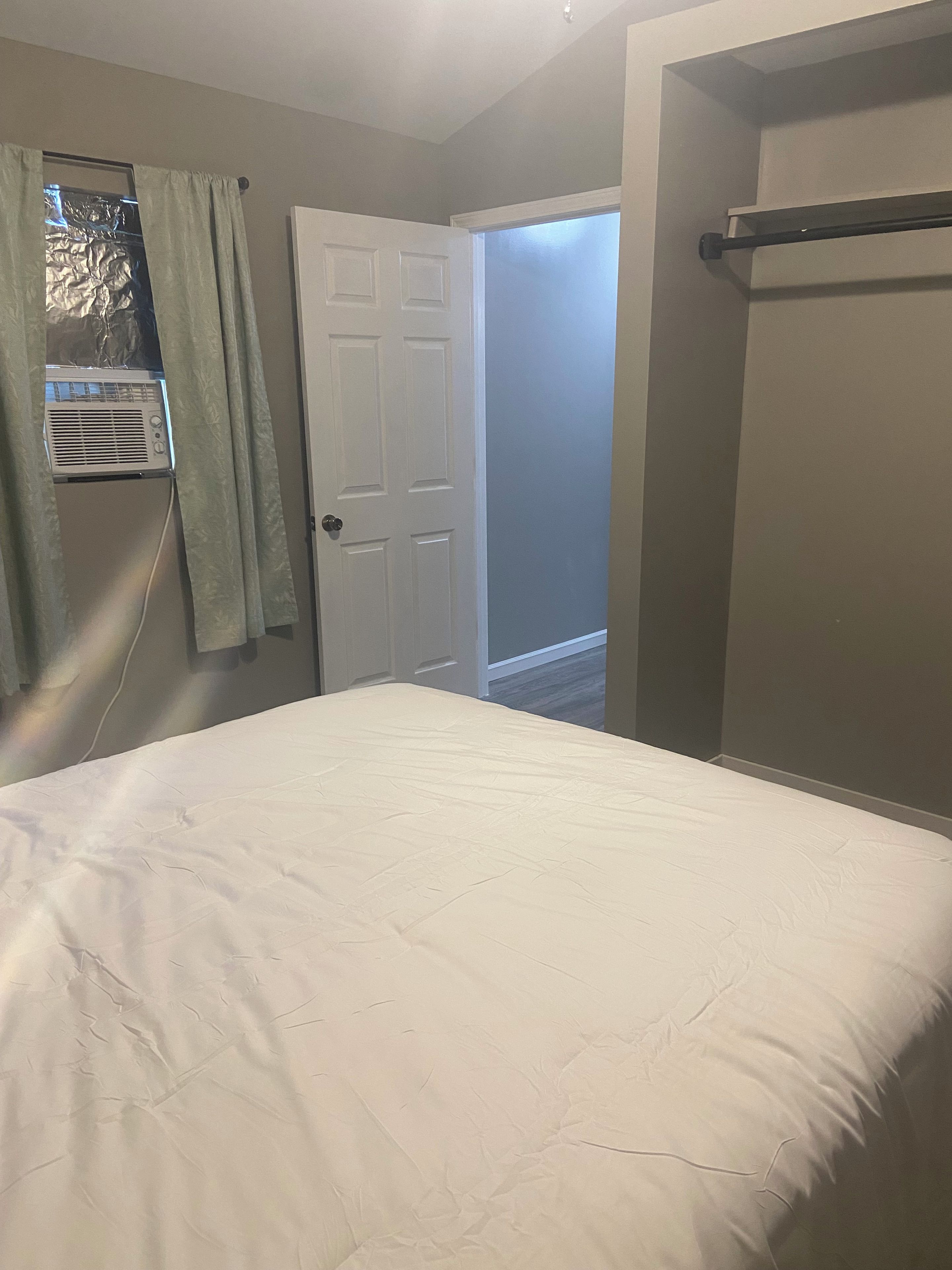 Un dormitorio con cama, puerta y ventana con cortinas.