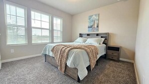 Ein Schlafzimmer mit einem Bett, Nachttischen, einem Gemälde und großen Fenstern.