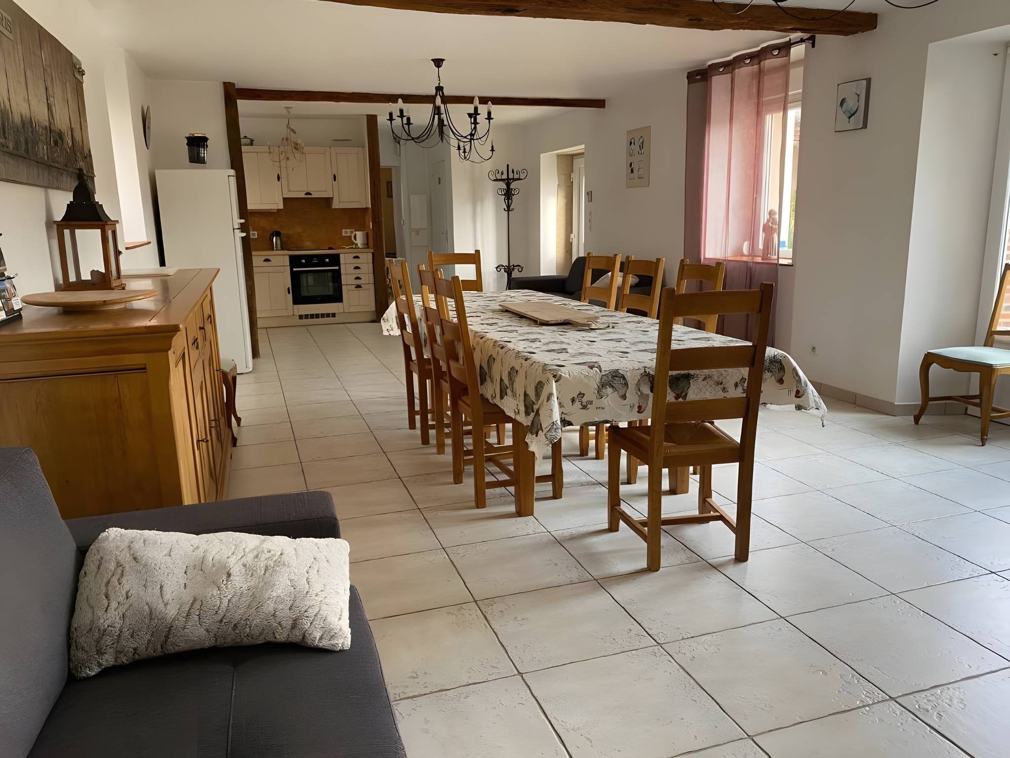 A spacious dining area with a long table and chairs, a kitchen in the background, and a cozy seating area with a sofa.