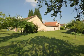 Een huis met een schuin dak, omgeven door een verzorgd gazon en bomen.