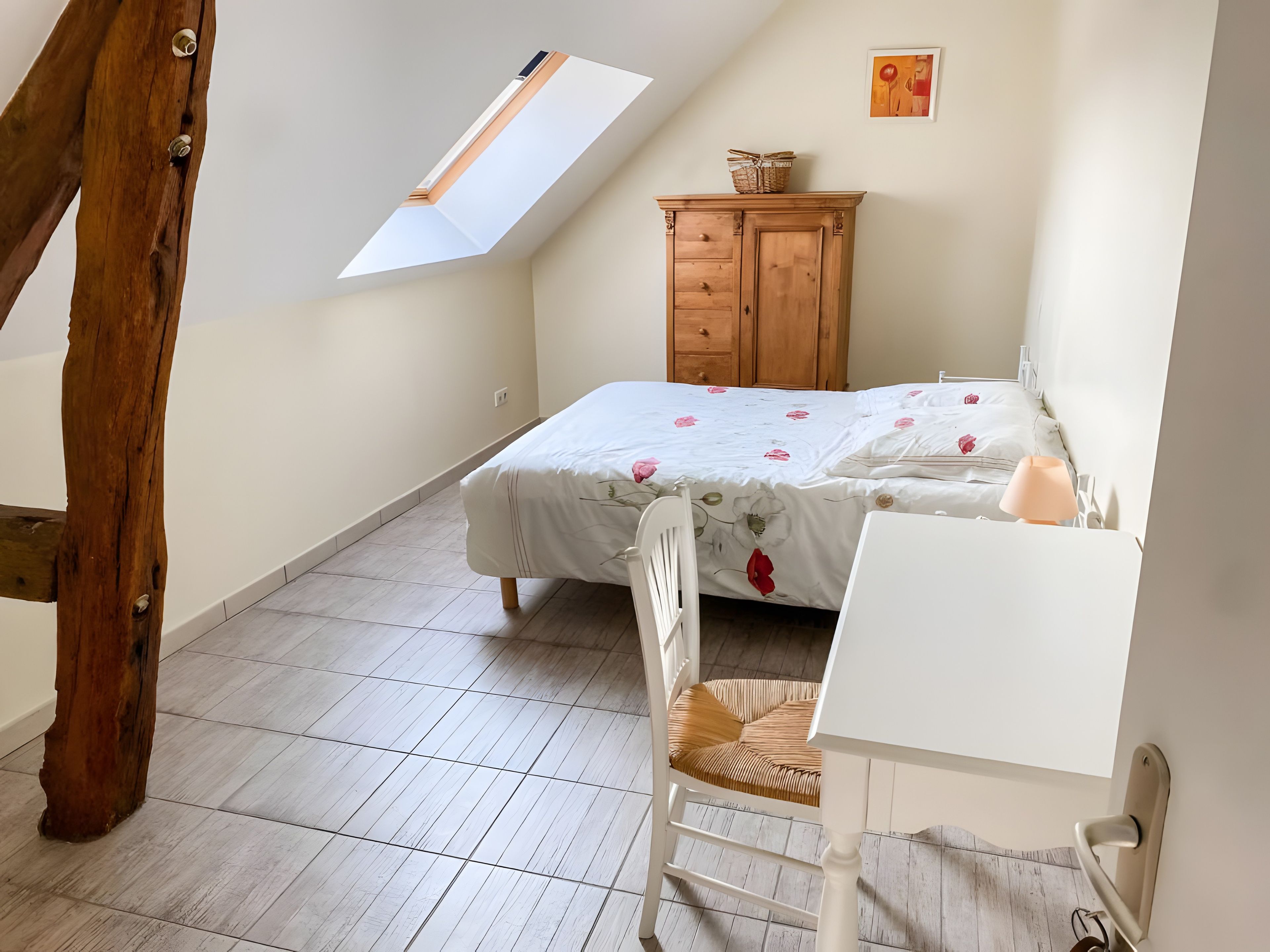 A bedroom with a sloped ceiling, a bed with floral bedding, a wooden dresser, a white desk, and a chair.
