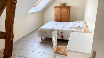A bedroom with a sloped ceiling, a bed with floral bedding, a wooden dresser, a white desk, and a chair.