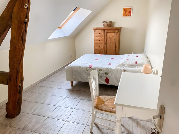 A bedroom with a sloped ceiling, a bed with floral bedding, a wooden dresser, a white desk, and a chair.