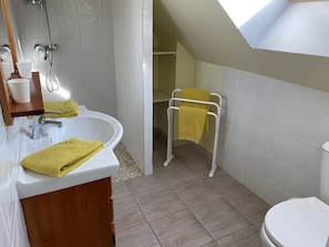 A modern bathroom with a white sink, a toilet, and a shower. There are yellow towels on the sink and a towel rack with a yellow towel.