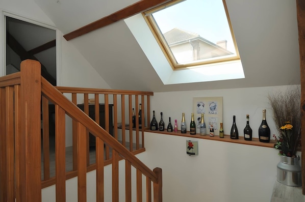 A wooden staircase leading to a room with a skylight, a wine rack with various bottles, and a framed picture on the wall.