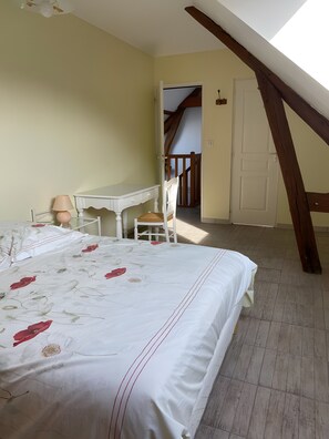 A bedroom with a bed, a desk, and a chair. There is a door and a staircase visible in the background.