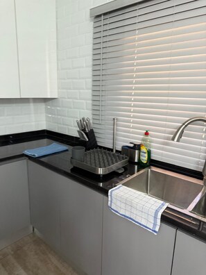 A kitchen with a black countertop, a waffle maker, a sink, and a window with blinds. - Cozy 2-bedroom apartment in brilliant Lusaka with AC (Lusaka)