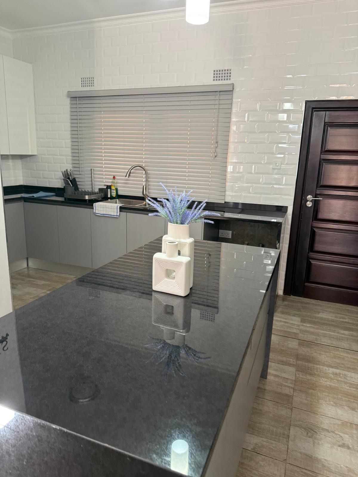 A modern kitchen with a central island, a built-in oven, and a window with blinds.