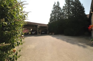 Ein überdachter Parkbereich mit Kiesbelag, ein geparktes Auto und ein Gebäude mit einem Ziegeldach im Hintergrund.