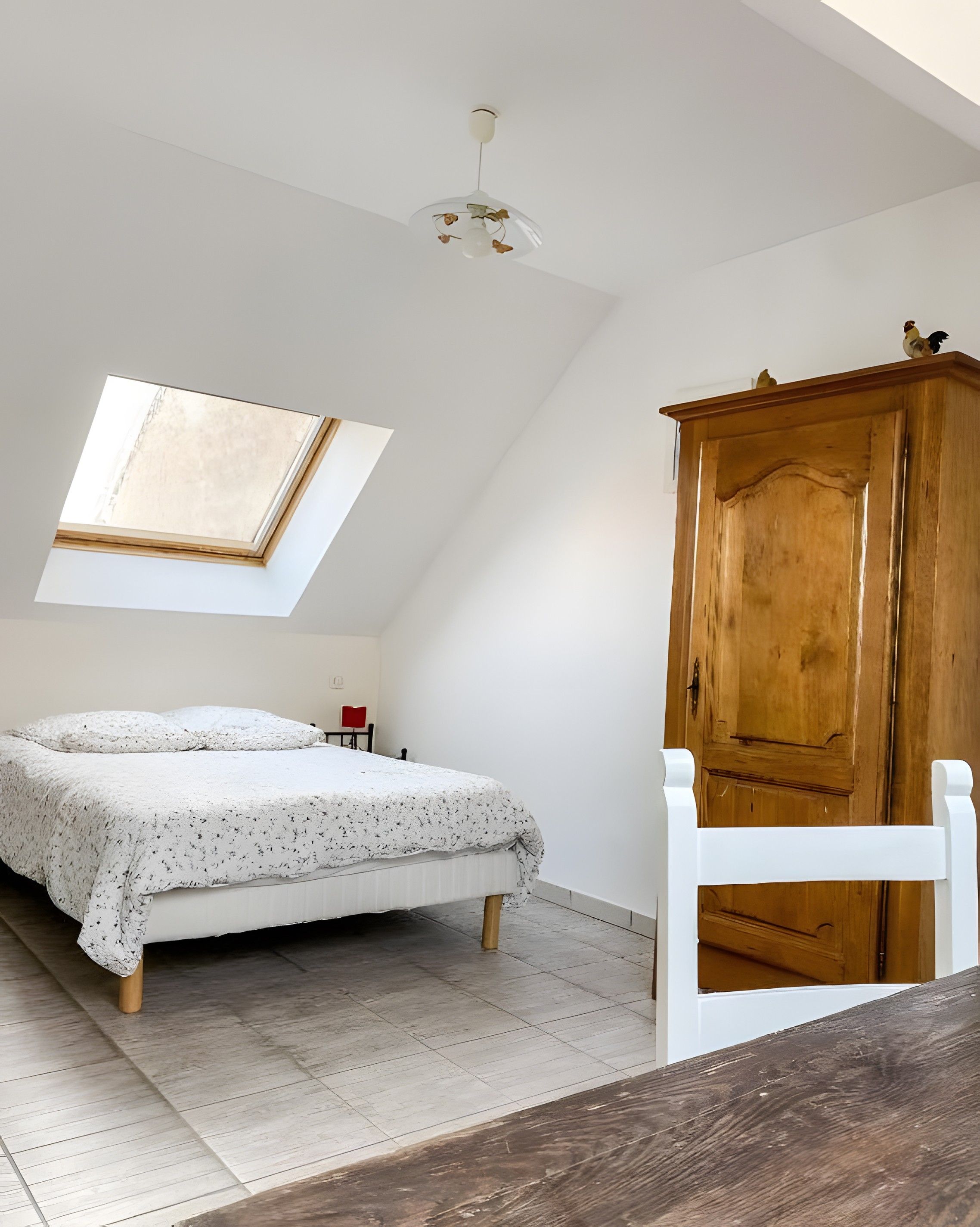 Een slaapkamer met dakraam, een bed, een houten garderobe en een rode stoel.