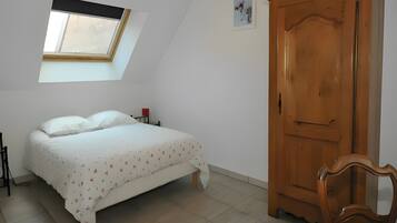 A bedroom with a bed, a wooden wardrobe, a red chair, a skylight, and a small wall decoration.
