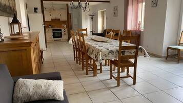A spacious dining area with a long table and chairs, a kitchen in the background, and a cozy seating area with a sofa.