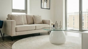 En moderne stue med en beige sofa, et glasbord og en hvid måtte.