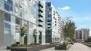 A modern multi-story building with large windows and balconies, surrounded by a landscaped area with trees and planters. - Modern 2-Bed Greenwich Apartment Fast Links to Canary Wharf (London)