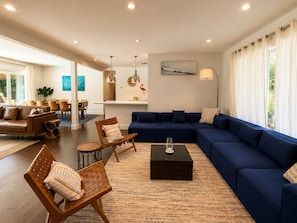 Een ruime woonkamer met een blauwe bank, een salontafel en een eethoek met stoelen en een tafel.