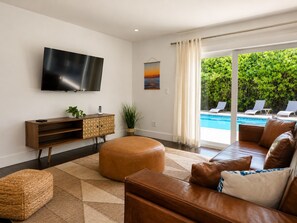 Una sala moderna con un televisor de pantalla plana, un sofá, un reposapiés y vistas a una piscina.