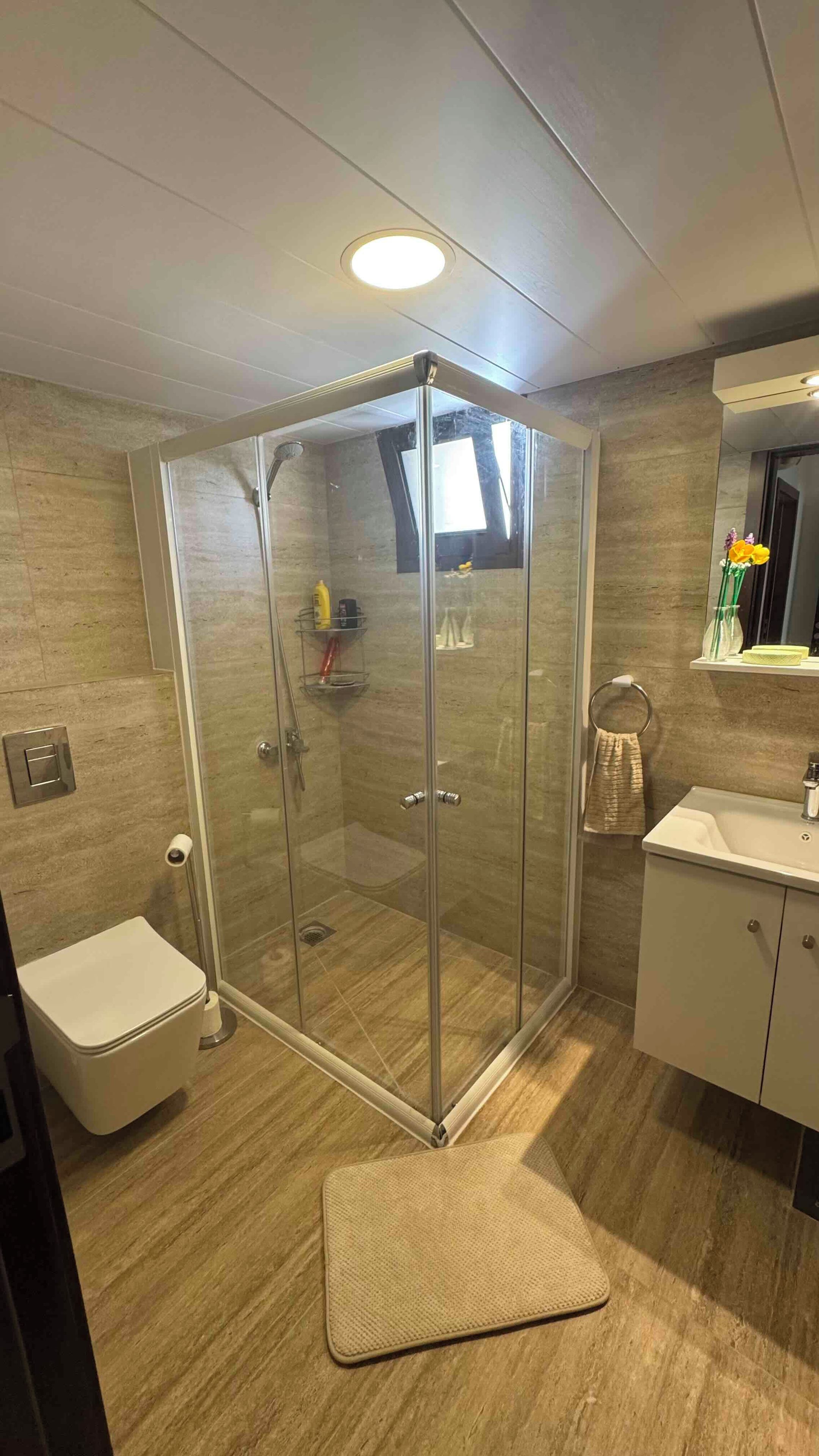 Un baño moderno con ducha acristalada, inodoro, lavabo y espejo.