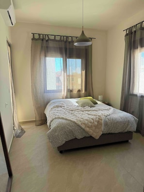 A bedroom with a bed, curtains, a hanging light fixture, and a window. - Cozy Corners- 2 bedroom apartment in amazing Byblos (byblos)