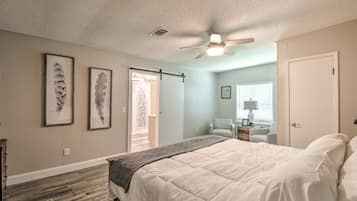 Quarto com cama, ventilador de teto e duas penas emolduradas na parede.