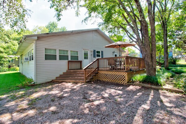A single-story house with a deck, a staircase leading to the deck, and a gravel driveway.