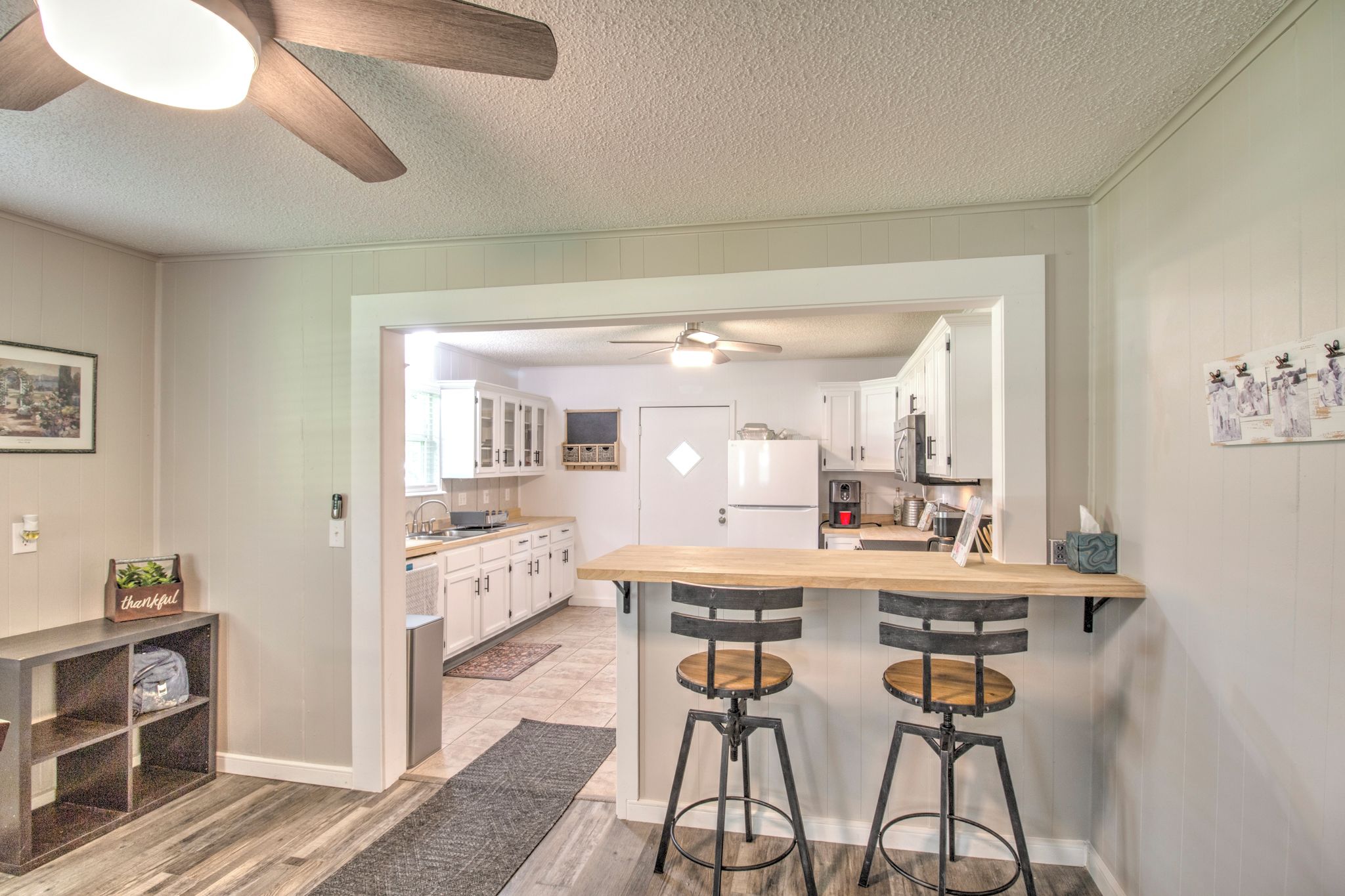 Une cuisine avec un bar en bois et deux tabourets, un ventilateur de plafond et un réfrigérateur.