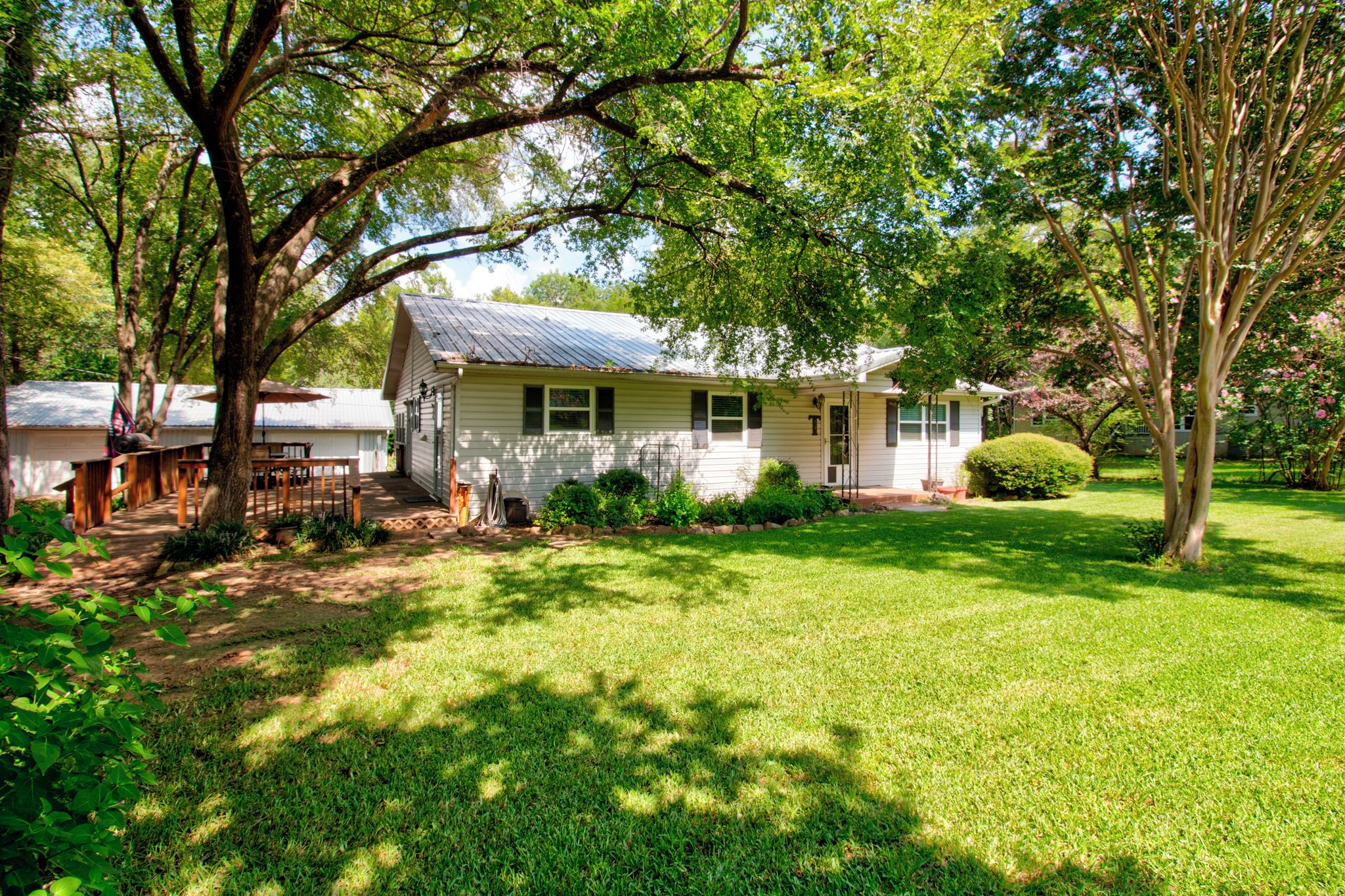 A single-story house with a front porch, surrounded by a well-maintained lawn and trees.