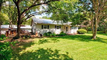 A single-story house with a front porch, surrounded by a well-maintained lawn and trees.