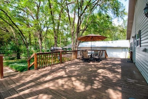 A wooden deck with a table and chairs, surrounded by trees and a white building.