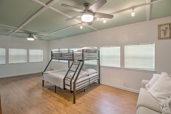Una habitación con literas, ventilador de techo y varias ventanas con persianas.