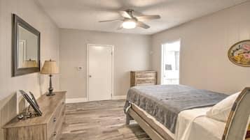 Une chambre à coucher comprenant un lit, une commode, un miroir, une lampe, un ventilateur de plafond et une porte.
