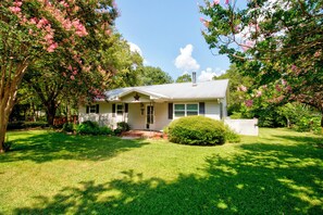 A single-story house with a front porch, surrounded by a well-maintained lawn and flowering trees.