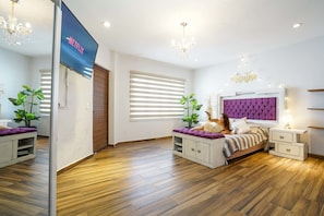 A modern bedroom with a large bed, a TV, and a chandelier.