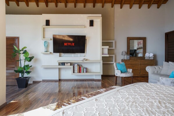Un dormitorio moderno con una cama grande, un televisor montado, una planta en maceta y un techo de madera.