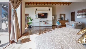 Een moderne slaapkamer met een groot bed, een aan de muur bevestigde televisie, een bank en een potplant.