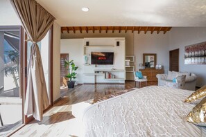 Quarto moderno com uma cama grande, televisão na parede, sofá e um vaso com planta.