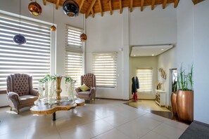 Un amplio salón con dos sillones cómodos, una mesa de centro de vidrio y ventanas grandes con persianas.