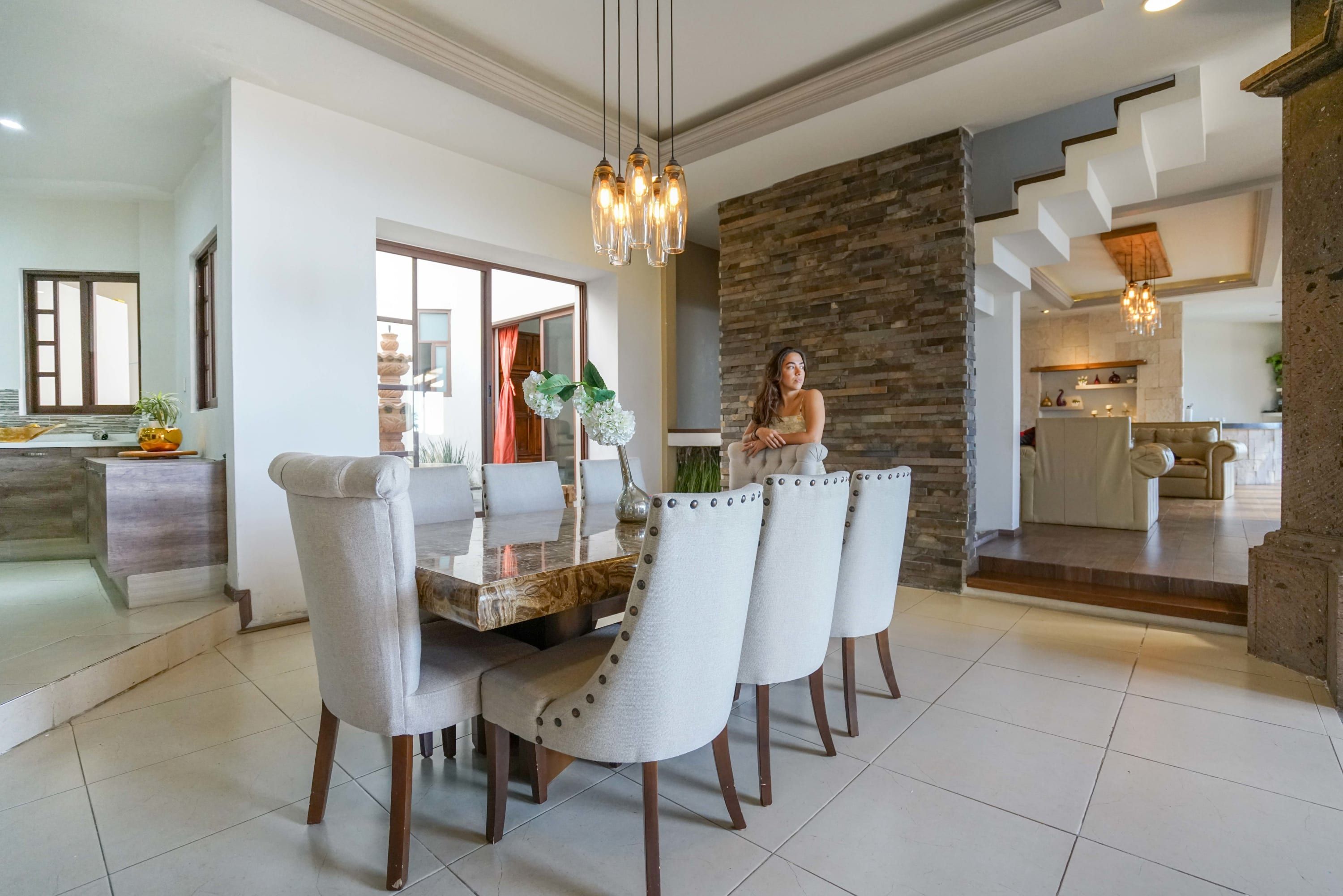 Un espace de salle à manger moderne, avec une table en marbre, des chaises à revêtement blanc et un mur d’accent en pierre.