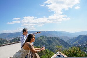 Um casal observa uma paisagem montanhosa a partir de uma varanda com piscina.