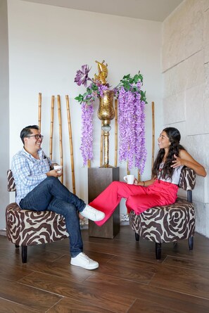 Two people seated on patterned chairs in a room with a decorative wall and a bamboo structure.