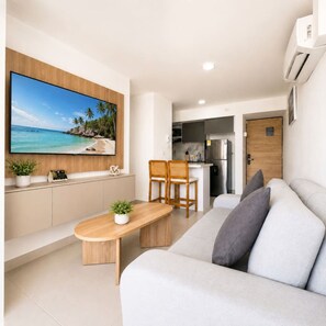 A modern living room with a large flat-screen TV, a wooden coffee table, a sofa, and a kitchen area in the background. - Sunlit Haze | 3BR,Beach, Sea View & Pool (Cartagena)