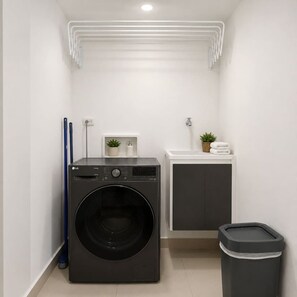 A compact laundry room with a front-loading washing machine, a small sink, and a trash bin. - Sunlit Haze | 3BR,Beach, Sea View & Pool (Cartagena)