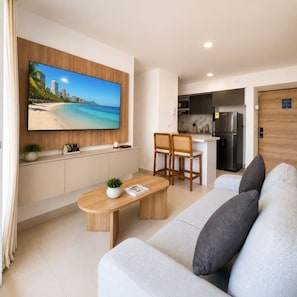 A modern living room with a flat-screen TV, a sofa, a coffee table, and a kitchen area in the background. - Sunlit Haze | 3BR,Beach, Sea View & Pool (Cartagena)