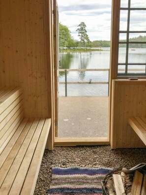 A wooden interior with a bench, a rug, and a view of a lake through a glass door. - Lakeside cabin at Älmtasjön with sauna & hot tub (Asarum)