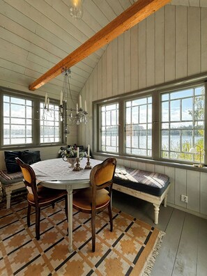 A dining area with a round table, chairs, a bench, and a view through large windows. - Lakeside cabin at Älmtasjön with sauna & hot tub (Asarum)