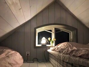 A bedroom with a sloped ceiling, a window with a white frame, a bedside table, and a bed with a white duvet. - Lakeside cabin at Älmtasjön with sauna & hot tub (Asarum)